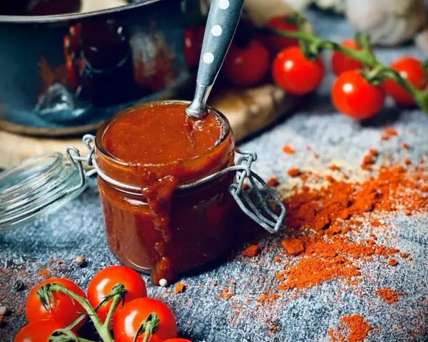 Ein Glas mit selbstgemachter bbq sauce, daneben Kirschtomaten und Paprikapulver. Perfekt für den Grill!