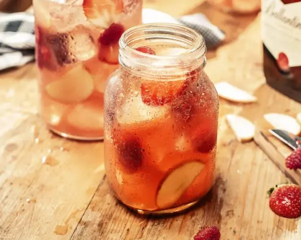 Orzeźwiający, kobiecy drink z whisky, pełen truskawek i jabłek, na drewnianym blacie.