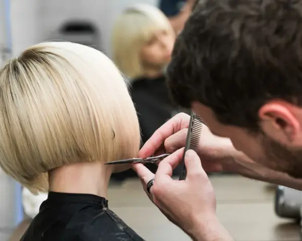 Fryzjerka tworzy modne fryzury odmładzające po 40 krótkie. Blond bob jest precyzyjnie cięty.