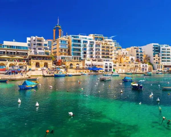 Malta, gdzie na Malcie jest tak pięknie! Woda krystalicznie czysta, łodzie kołyszą się na falach, a w tle kolorowe budynki.