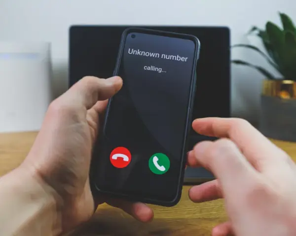 Dłoń trzyma telefon, na ekranie którego widnieje komunikat "Unknown number calling...". Czy odbierze, gdy numer prywatny dzwoni?