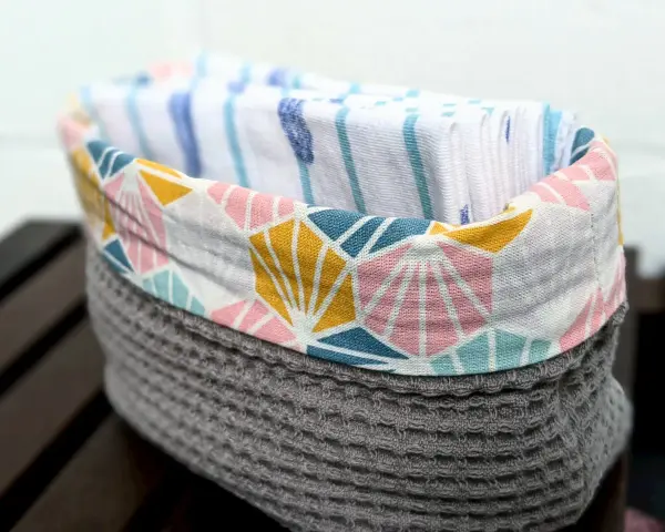 Un panier en tissu gris avec un motif géométrique coloré contient des mouchoirs en tissu. Une idée pour savoir que faire avec des mouchoirs en tissu.