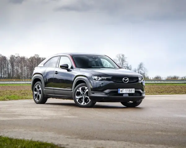 Czarna Mazda MX-30 na tle pochmurnego nieba i drzew.