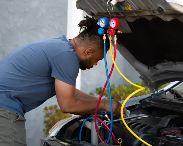 Man working on car engine, using gauges and hoses to fix car AC.