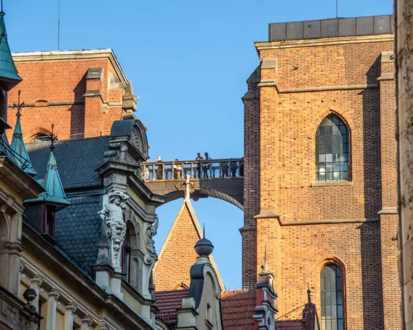 Most zabytkowych budynków we Wrocławiu z ludźmi na moście i wieżą Katedry w tle.