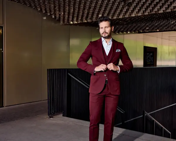 Elegancki mężczyzna w bordowym garniturze i marynarce zapina guziki.