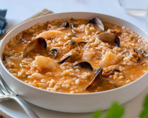 Un delicioso arroz caldoso de marisco, repleto de gambas, mejillones y almejas, servido en un cuenco blanco.