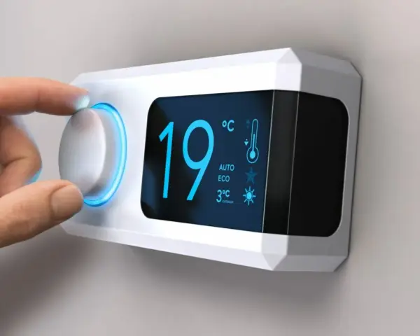 Main d'une personne ajustant le réglage de température sur un cee thermostat connecté affichant 19°C.