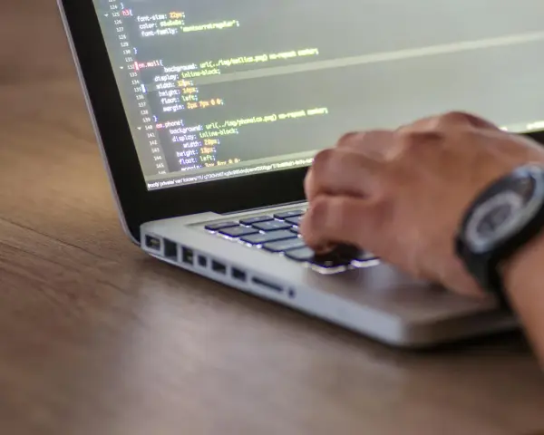 Kodowanie strony internetowej, widać fragment kodu HTML z listą nieuporządkowaną i rękę piszącą na klawiaturze.