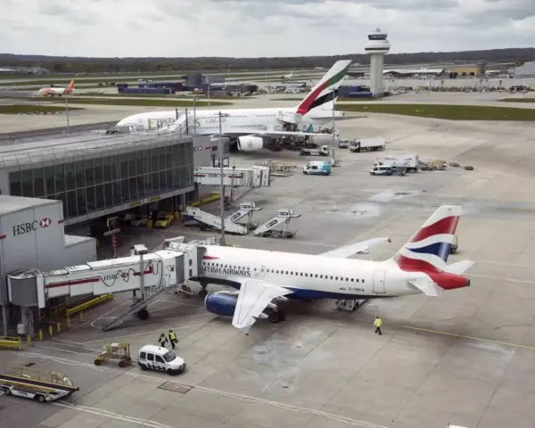 Samoloty British Airways i Emirates czekają na pasażerów na lotnisku Gatwick. W tle widać wieżę kontroli lotów.
