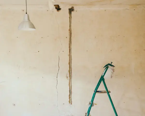 Pękające ściany starego domu, widoczna instalacja elektryczna i drabina.
