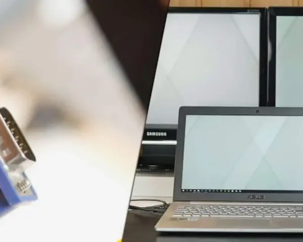 Ein VGA-Kabel wird verwendet, um einen Laptop mit einem Bildschirm zu verbinden. Mehrere Monitore sind im Hintergrund zu sehen.