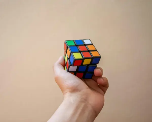 En hand håller en färgglad rubiks kub nyckelring mot en ljus bakgrund.