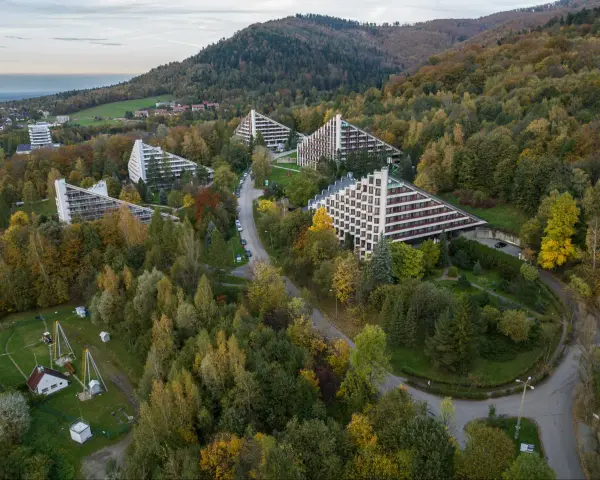 Widok z lotu ptaka na sanatoria o trójkątnej architekturze w otoczeniu jesiennego lasu.