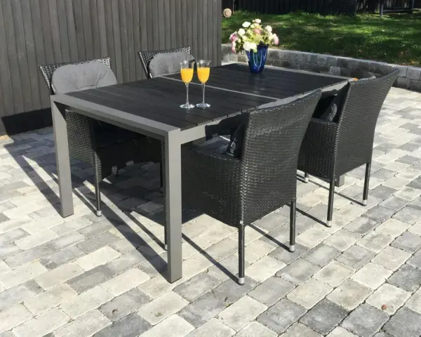 En uteplats med stenläggning, ett mörkt bord med korgstolar och glas med juice.