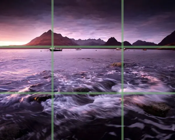 Paysage marin au crépuscule, avec des montagnes en arrière-plan et des bateaux sur l'eau. La composition suit la règle des tiers pour un équilibre visuel.