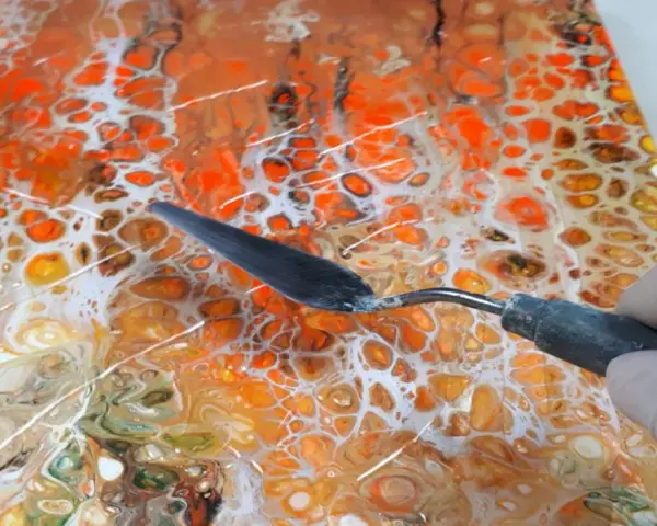 Maintenant, peut-on mettre de la résine sur de la peinture acrylique ? Un outil est utilisé pour travailler une peinture abstraite aux couleurs vives, orange et blanc.
