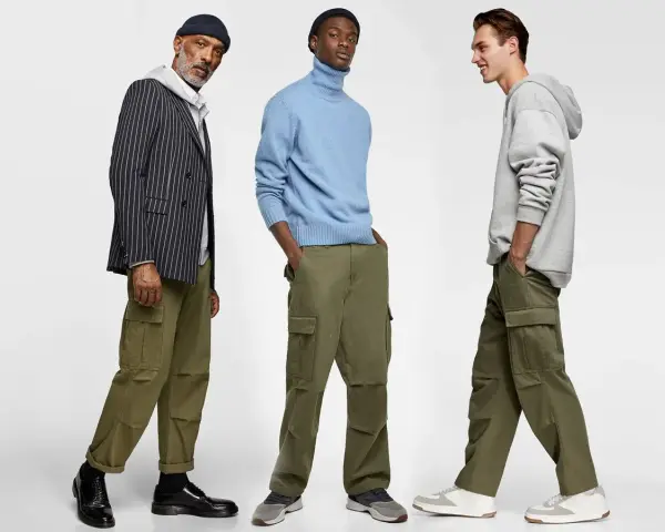 Tres hombres posan con pantalones cargo y camisas. Uno lleva un blazer a rayas, otro un suéter azul y el tercero una sudadera gris.