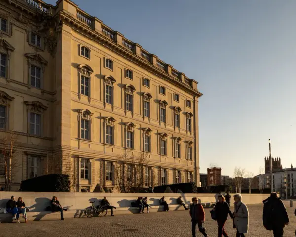 Sonnenlicht beleuchtet das barocke Gebäude, ein schönes Beispiel für kostenlose Orte, die man in Berlin besuchen kann. Menschen entspannen sich auf einer Bank.
