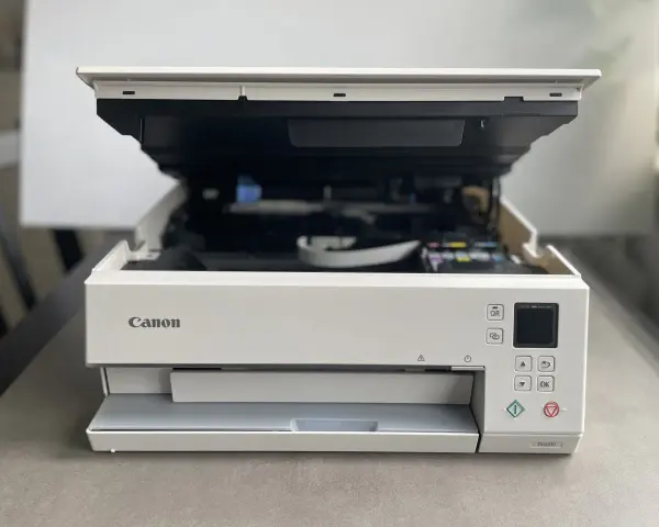 Biała drukarka Canon z otwartą pokrywą, widoczne tusze. Poradnik jak zainstalować drukarkę Canon.