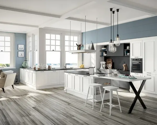 Cucina luminosa con isola centrale, sgabelli bianchi e una nicchia sotto finestra con vista mare.