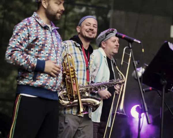 Adam Kłosiński z zespołem na scenie, grają na saksofonie i puzonie.