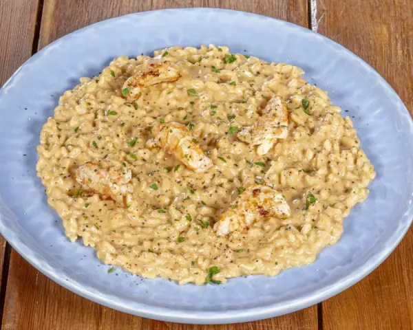 Un cremoso risotto alla crema di scampi, guarnito con scampi scottati e prezzemolo tritato, servito su un piatto azzurro.