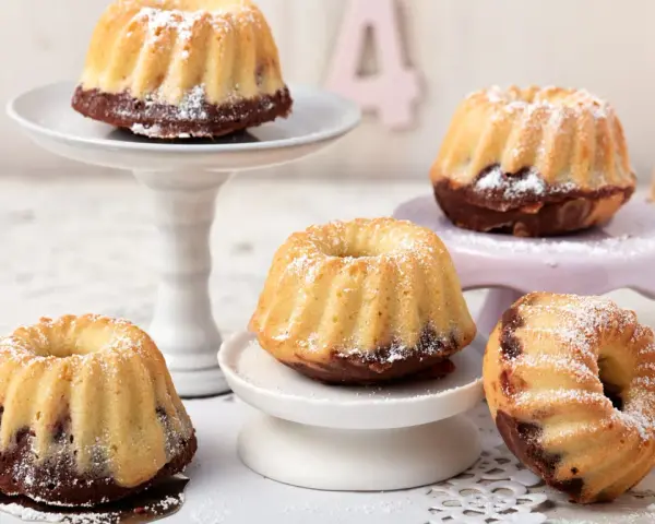 Mehrere mini Gugelhupf mit Puderzucker bestäubt, auf verschiedenen Etageren arrangiert.