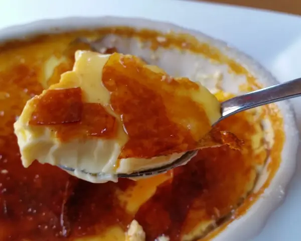 En sked tar en bit av en krämig creme brulee med karamelliserat socker. Perfekt dryck till creme brulee.