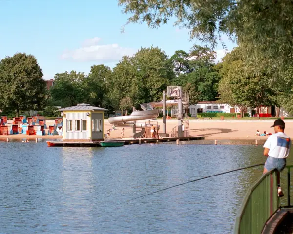 Am Orankesee Strandbad tummeln sich Badegäste, während ein Angler geduldig auf seinen Fang wartet.