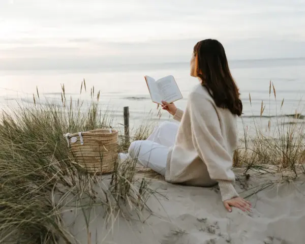 Kobieta czyta książkę na plaży, ciesząc się spokojem i świeżym powietrzem. To idealny moment, by poczuć, kiedy jest najwięcej jodu nad morzem.