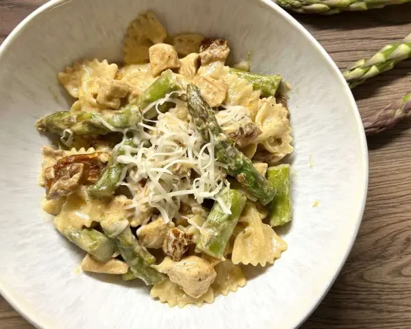 Pyszne makaron farfalle ze szparagami i kurczakiem w kremowym sosie, posypany startym parmezanem.