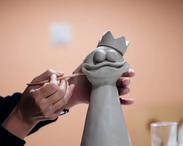 Manos trabajando con arcilla para crear una figura de rana con corona.