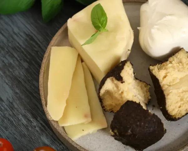 Różnorodne rodzaje serów na talerzu: kawałki żółtego sera, kulka mozzarelli i ser w ciemnej skórce.