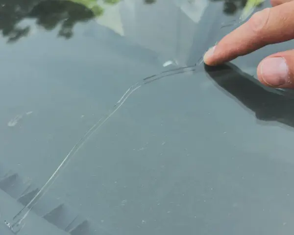Palec wskazujący na pękniętej szybie samochodowej. Sprawdź autoglass cennik, aby poznać koszt naprawy.