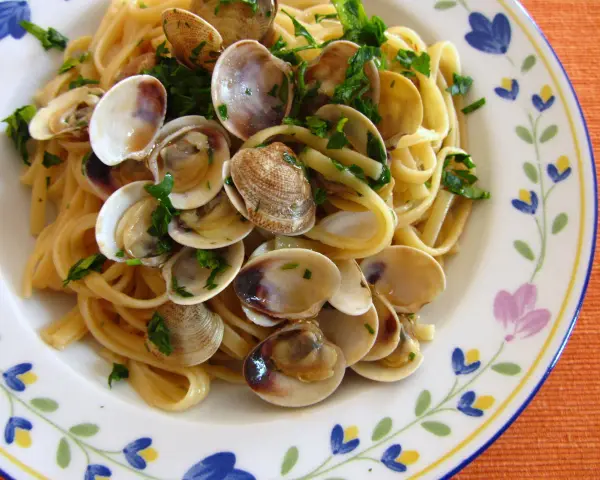Pyszne spaghetti vongole z małżami i natką pietruszki na talerzu z kwiatowym wzorem.