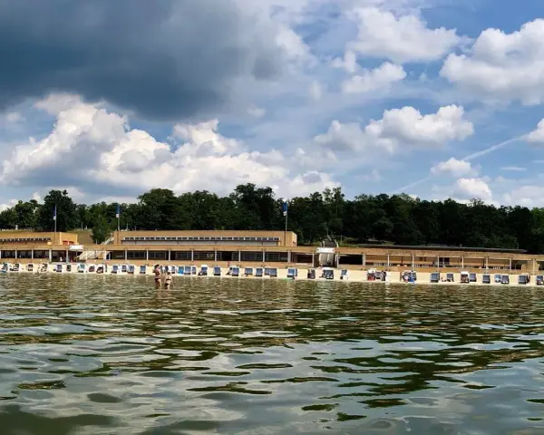 Das Strandbad Wannsee mit seiner langen Promenade und vielen Liegestühlen, im Hintergrund grüne Bäume und ein bewölkter Himmel.