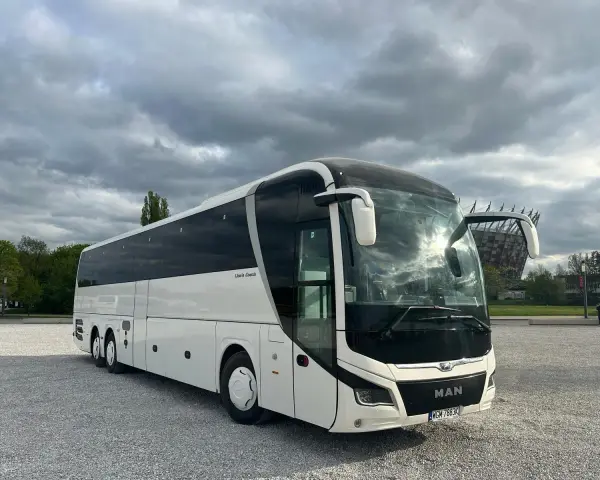 Biały MAN Lion's Coach, nowoczesny autokar turystyczny, zaparkowany na żwirowym placu pod pochmurnym niebem.