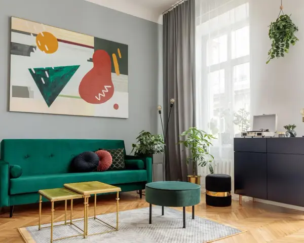 Soggiorno moderno con divano verde smeraldo e tavolini dorati. L'arte astratta sul muro grigio e i mobili scuri creano un perfetto abbinamento colori pareti e mobili.