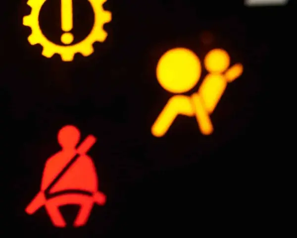 Das gelbe airbag symbol leuchtet. Daneben ein rotes Symbol für den Sicherheitsgurt. Ein gelbes Zahnrad mit Ausrufezeichen ist oben links zu sehen.