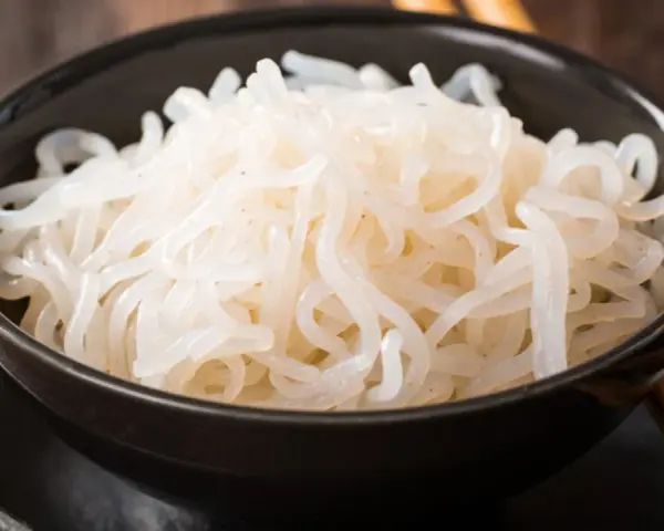 Misternie ułożony makaron konjac w czarnej misce, gotowy do spożycia z pałeczkami.