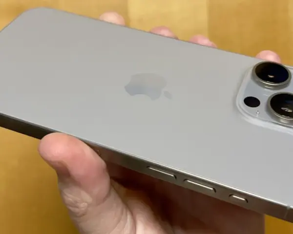 En hand håller en silverfärgad iPhone 15 Pro Max. Kameramodulen med tre linser syns tydligt.