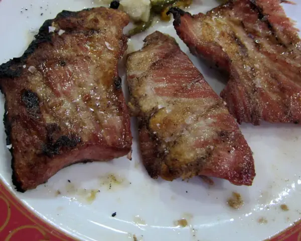 Tres trozos de secreto de cerdo a la parrilla, jugosos y con sal gruesa, servidos en un plato blanco con borde rojo.