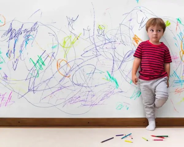 Chłopiec z ADHD, stojący przy ścianie pokrytej kolorowymi bazgrołami, wyraża swoje emocje.