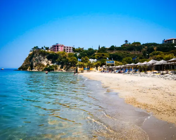 Piękne, turkusowe morze na Zakynthos. Plaża z leżakami i parasolami, a na klifie hotel.