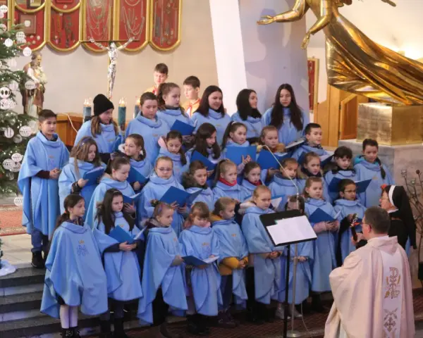 Dzieci w błękitnych strojach tworzą schola, śpiewając w kościele przy choince.