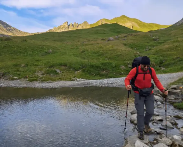Un randonneur traverse un ruisseau de montagne, bâtons en main. Une belle illustration de pourquoi marcher avec des bâtons pour plus de stabilité.