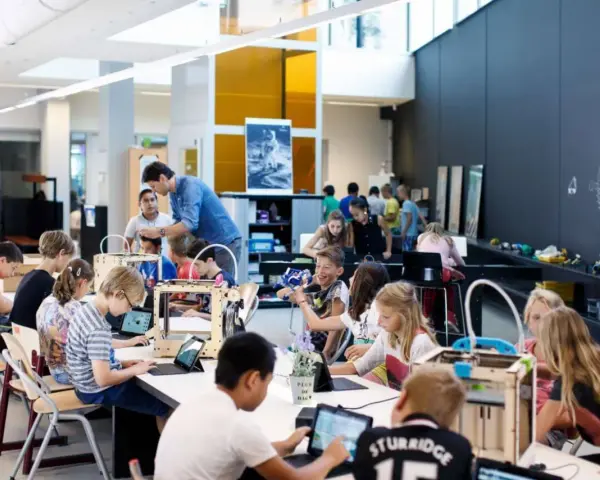 Children engage in 3d printing education, working with laptops and 3D printers in a bright, modern classroom.