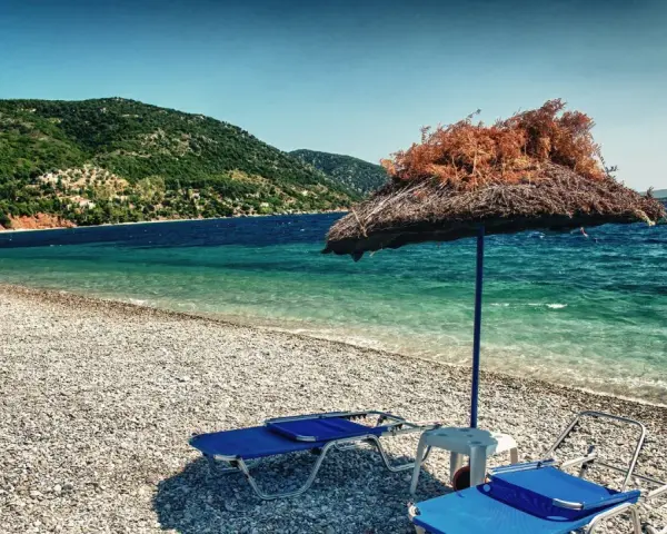 Plaża z leżakami i parasolem, w tle zielone wzgórza i turkusowe morze. To idealne miejsce na wypoczynek na grupie wysp na Morzu Egejskim.