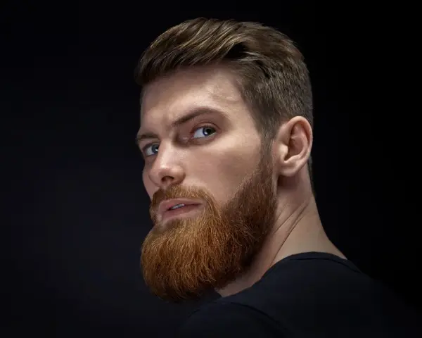 Hombre con barba rojiza y peinado actual, con el pelo peinado hacia atrás y un corte moderno.